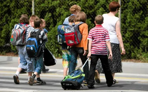 Niños con mochilas y un carrito cruzan la calle, marcando el regreso a la rutina de septiembre.