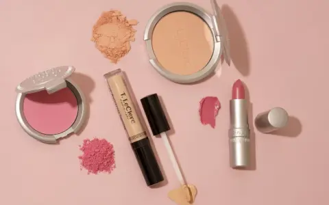 Un assortiment de maquillage rose et doré : blush, poudre, fond de teint, rouge à lèvres et fard à paupières sur fond rose.