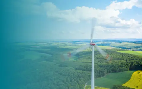 Windkraftanlage im Vordergrund, die sich dreht. Im Hintergrund eine Landschaft mit weiteren Anlagen, die die Amortisation der Windkraftanlage symbolisieren.