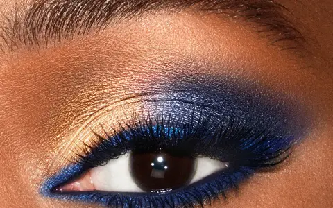 Un œil aux smoky eyes bleus intenses, rehaussé de fard doré et de paillettes. Un regard captivant.