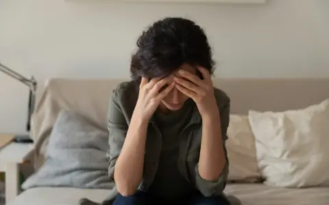 A woman sits with her head in her hands, overwhelmed by the cycle of self-destruction.