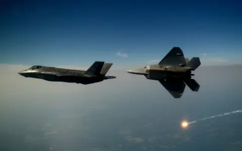 Zwei Tarnkappen-Kampfflugzeuge, ein F-35 und ein F-22, fliegen im Tandem über den Wolken. Ein F-22 schießt eine Leuchtrakete ab.