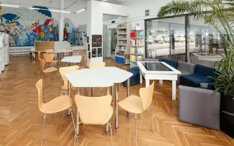 Spazi della scuola luminosi con scaffali, tavoli, sedie e un murale colorato. Un'area accogliente per imparare e giocare.