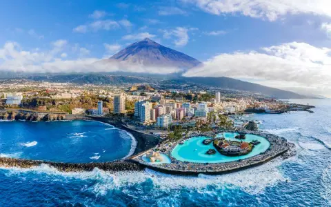 Città costiera con piscina a sfioro e vulcano sullo sfondo. Un'ottima idea su dove andare ad aprile per una vacanza al mare.