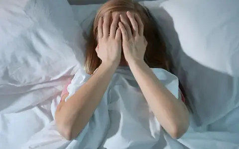 Dziewczyna w łóżku zakrywa twarz dłońmi, walcząc z bezsennością. Co to jest bezsenność?