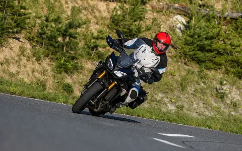Motocyklista w kasku na zakręcie górskiej drogi. Planujesz podróż na Korsykę? Sprawdź ceny paliwa i noclegów!