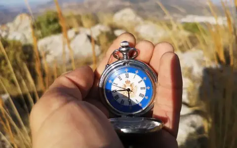 Mano sostiene un reloj de bolsillo antiguo con esfera azul y números romanos, útil para orientarse con reloj de agujas en un paisaje montañoso.