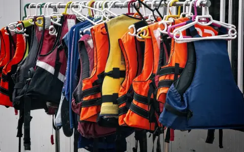 Chalecos salvavidas de varios colores, como naranja, amarillo y azul, colgados en perchas. Listos para la aventura, estos chalecos son de epis categoria 2.