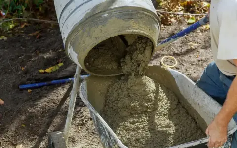 Betoniarka wylewa świeży beton do taczki. Widać, ile żwiru na metr sześcienny betonu jest w tej mieszance.