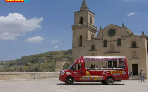 Un bus rosso "open top" per un tour di Matera, con la chiesa e i Sassi sullo sfondo.