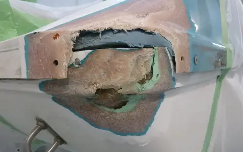 Beschädigte Stelle an einem GFK Boot, bereit für die Reparatur. Die Fasern sind freigelegt, ein Zeichen für notwendige Instandsetzung.