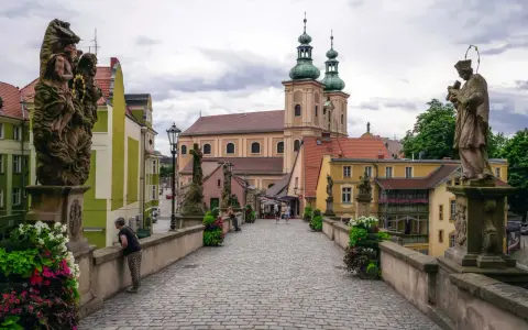 Kamienna, brukowana ścieżka prowadzi do barokowego kościoła z zielonymi wieżami. Wzdłuż mostu stoją kamienne rzeźby. To piękne ziemia kłodzka atrakcje.