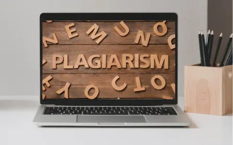 Laptop z napisem "PLAGIARISM" ułożonym z drewnianych liter na tle desek.