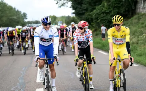 Radfahrer in bunten Trikots, Teil der Tour de France Teams, fahren auf der Straße. Einer trägt das Gelbe Trikot.