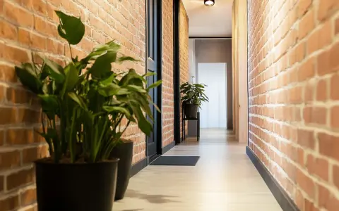 Przedpokój loft inspiracje: ceglane ściany, jasna podłoga, czarne drzwi i zielone rośliny tworzą przytulną przestrzeń.