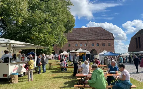 Sommerliche Zarrentin Veranstaltungen: Menschen genießen ein Fest mit Ständen und Sitzgelegenheiten im Freien vor historischen Gebäuden.