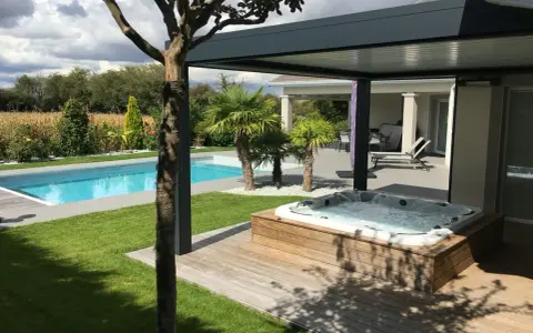 Un spa bouillonnant sur une terrasse en bois, à côté d'une piscine bleue. Le tableau temps de filtration piscine est visible dans le jardin luxuriant.