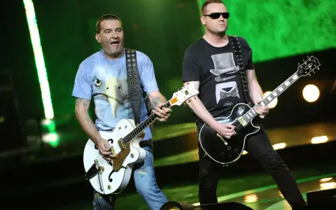 Dwóch członków Kobranocki gra na gitarach podczas koncertu. Jeden w koszulce z orłem, drugi w czarnej z cylindrem i muszką.