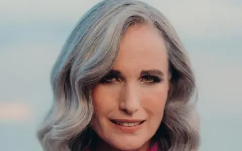 Mujer de 50 años con cabello plateado y ondulado, sonriendo suavemente. Se aprecian las líneas de expresión, reflejo de la flacidez facial a los 50.
