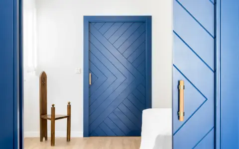 Puertas azules interiores con diseño geométrico y tiradores de madera. Una silla de madera antigua destaca junto a una de las puertas.