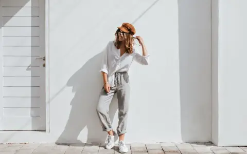 Modello con cappello marrone e occhiali da sole, indossa una camicia bianca e pantaloni grigi. Un esempio di abbinamenti outfit grigio casual e chic.