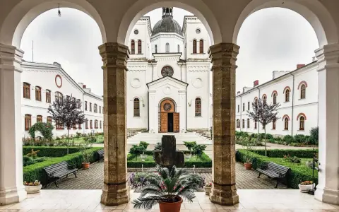 A courtyard with a cross and potted plants, framed by arches. The white church in the background is a place where monks like Father John and Brother Michael find peace.