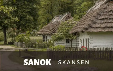 Skansen Sanok: tradycyjne chaty kryte strzechą, zielone drzewa i płot. Sprawdź cennik i zaplanuj wizytę!