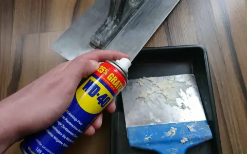 Spray WD-40 do czyszczenia zaschniętego betonu z narzędzi. Na zdjęciu puszka WD-40 i kielnia.