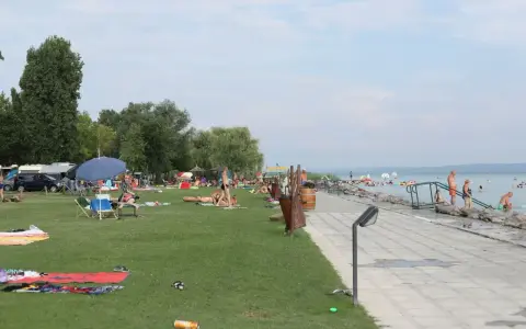 Ludzie odpoczywają na plaży i w wodzie. W tle widać kampery, co sugeruje, że to popularne miejsce na napfeny camping.