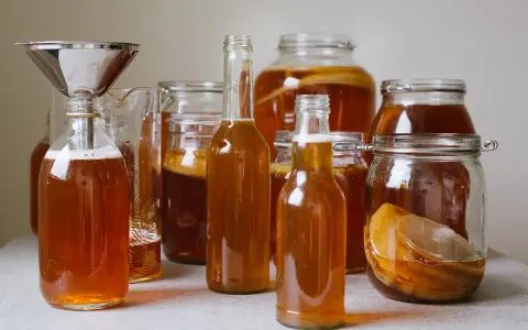Flera flaskor och burkar med gyllene kombucha, redo för andra jäsningen. Ett perfekt kombucha recept för hemmabruk.