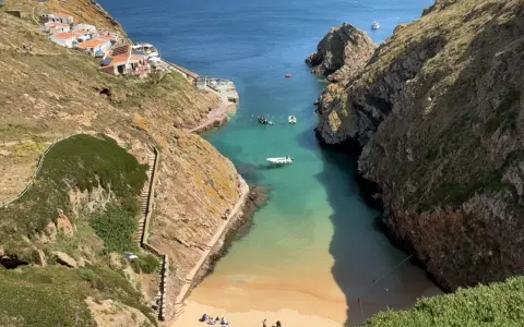 Idyllische Bucht mit weißem Sandstrand und türkisfarbenem Wasser auf den Berlengas Inseln. Kleine Boote ankern, Häuser schmiegen sich an die Felsen.
