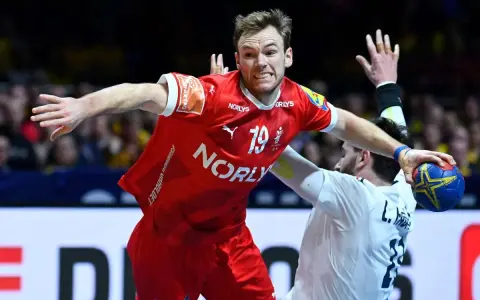 Mathias Gidsel w czerwonej koszulce z numerem 19, w akcji podczas meczu piłki ręcznej, walczy o piłkę.