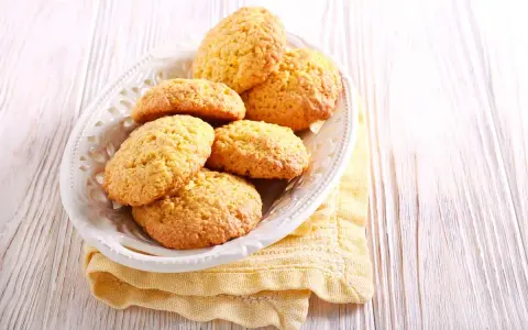 Biscotti con farina di mais dorati e friabili, serviti in un piatto bianco su un tovagliolo giallo.