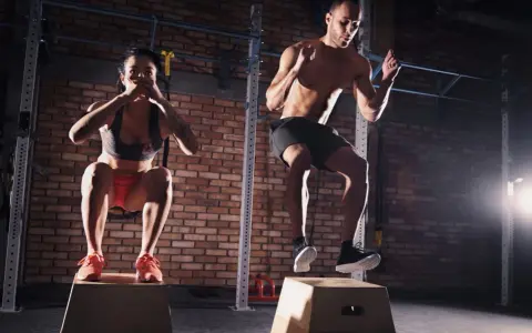 Para ćwicząca CrossFit wykonuje skoki na skrzyni w siłowni.