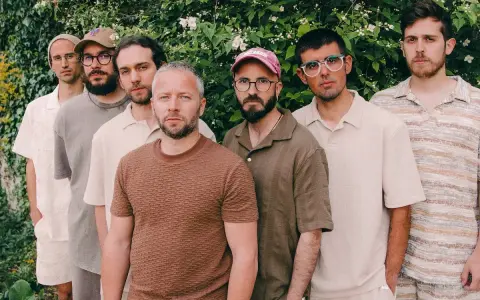 Los miembros de Oques Grasses posan juntos, con ropa de tonos tierra y un fondo de vegetación frondosa.
