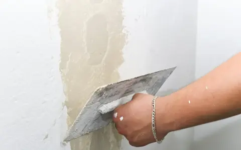 Main d'un artisan appliquant de l'enduit pour réparer une fissure crepis maison.