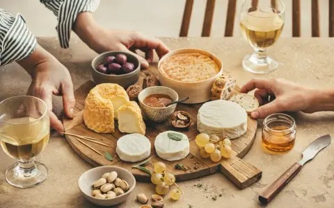 Un tableau accord vin et fromage avec divers fromages, olives, noix, raisins, pistaches et miel.
