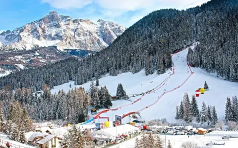 Ośnieżony stok narciarski w Alta Badia z lasem i górami w tle.