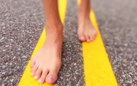 Piedi nudi che camminano su una strada con strisce gialle. Un'esperienza di correre scalzi per sentire la strada.