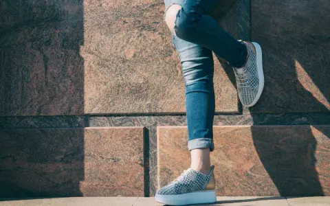 Kobieta w podartych jeansach i modnych sneakersach. Pokazano, jak podwinąć spodnie, by uzyskać stylowy efekt.