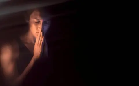 Młody mężczyzna w półmroku, z dłońmi złożonymi jak do modlitwy, szuka spokoju. Kiedy onanizm nie jest grzechem, a drogą do samopoznania.