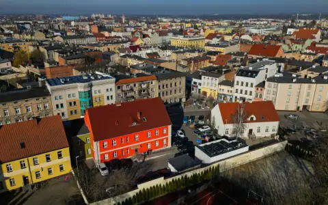 Widok z lotu ptaka na miasto, gdzie leży Ostrów Wielkopolski. Widać kolorowe kamienice, dachy i samochody.