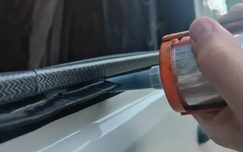 Application de mastic Sika 265 sur un joint de fenêtre de véhicule pour une étanchéité parfaite.