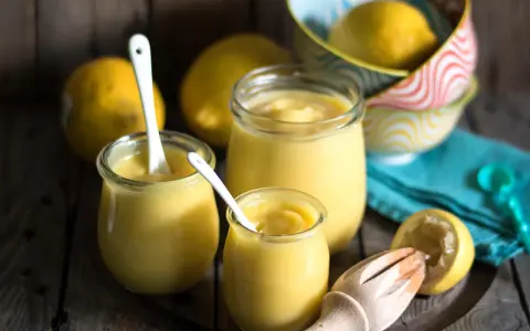 Drei Gläser mit cremigem Lemon Curd, Löffel und frische Zitronen. Perfekt für ein einfaches Lemon Curd Rezept.