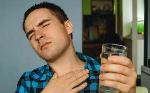 Mężczyzna z bólem gardła, cierpiący na nocny kaszel po alkoholu, sięga po szklankę wody.
