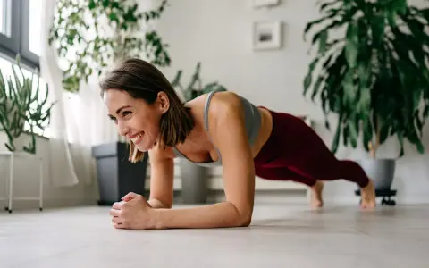 Femme souriante en plein exercice de gainage, profitant d'un moment de bien-être à la maison.