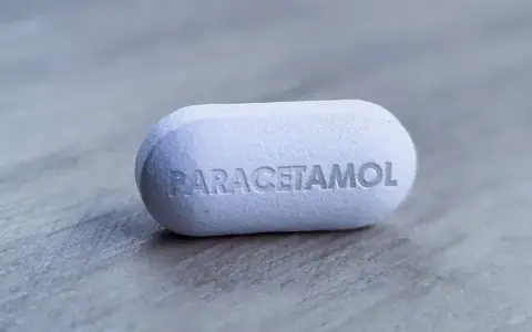 Biała tabletka z napisem "PARACETAMOL" na szarym tle. Dylemat: apap czy paracetamol?
