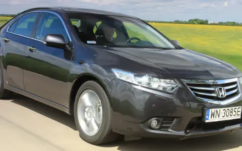 Ciemnoszary sedan Honda Accord, idealny auto do 40 tys., jedzie przez pola rzepaku.