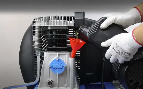 Wymiana oleju w sprężarce powietrza to kluczowy element jej naprawy. Ręce w białych rękawiczkach wlewają olej przez czerwony lejek.