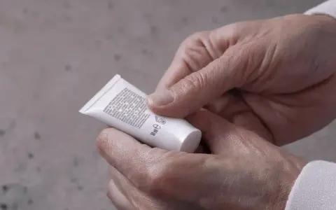 Mani che tengono un tubetto di crema, leggendo gli ingredienti che includono l'acido miristico, per una pelle nutrita.
